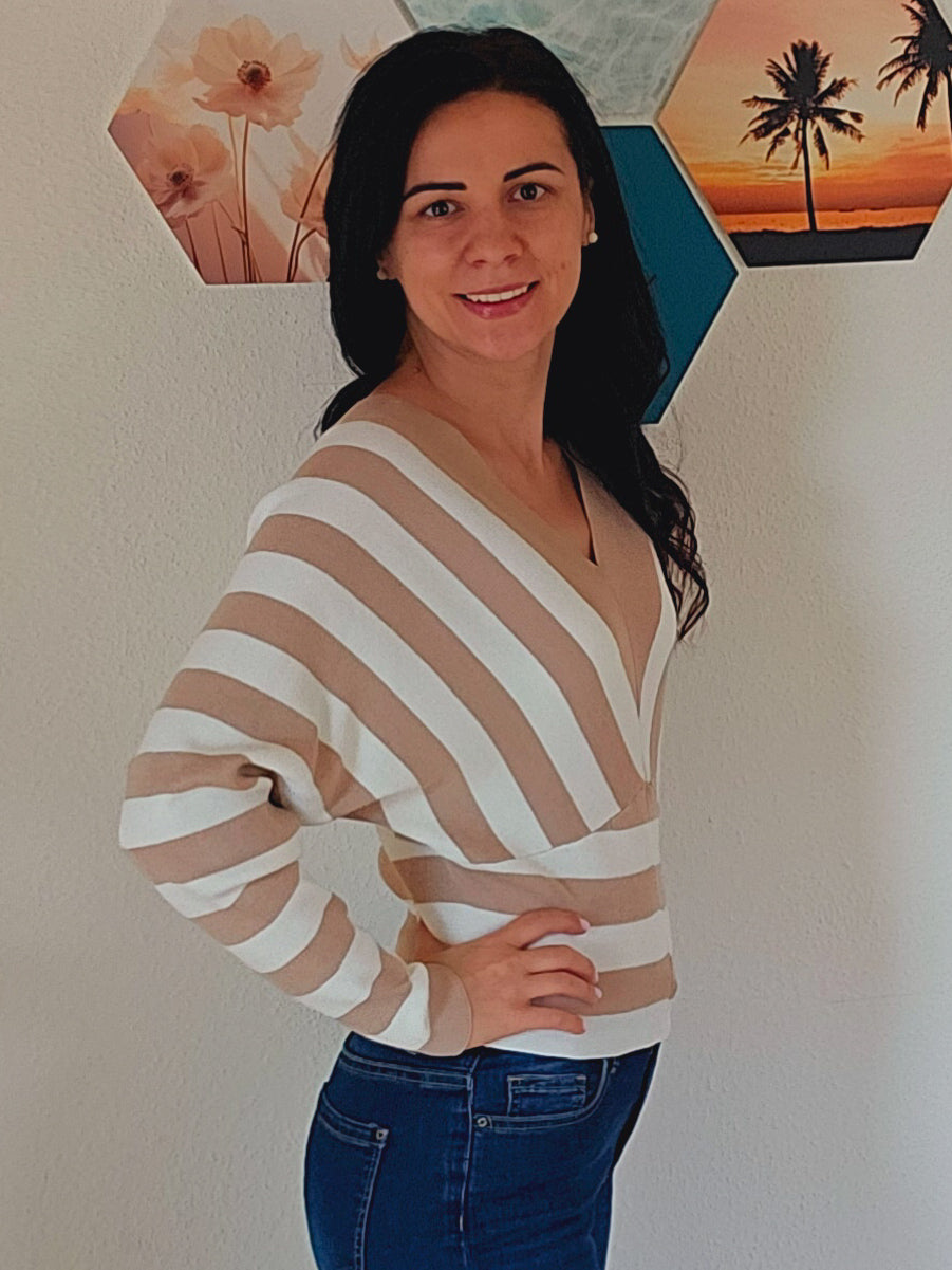 Das Model trägt einen gestreiften Pullover mit V-Ausschnitt in Beige und Weiß. Die breiten Streifen verlaufen diagonal und horizontal, was dem Oberteil ein interessantes Design verleiht.