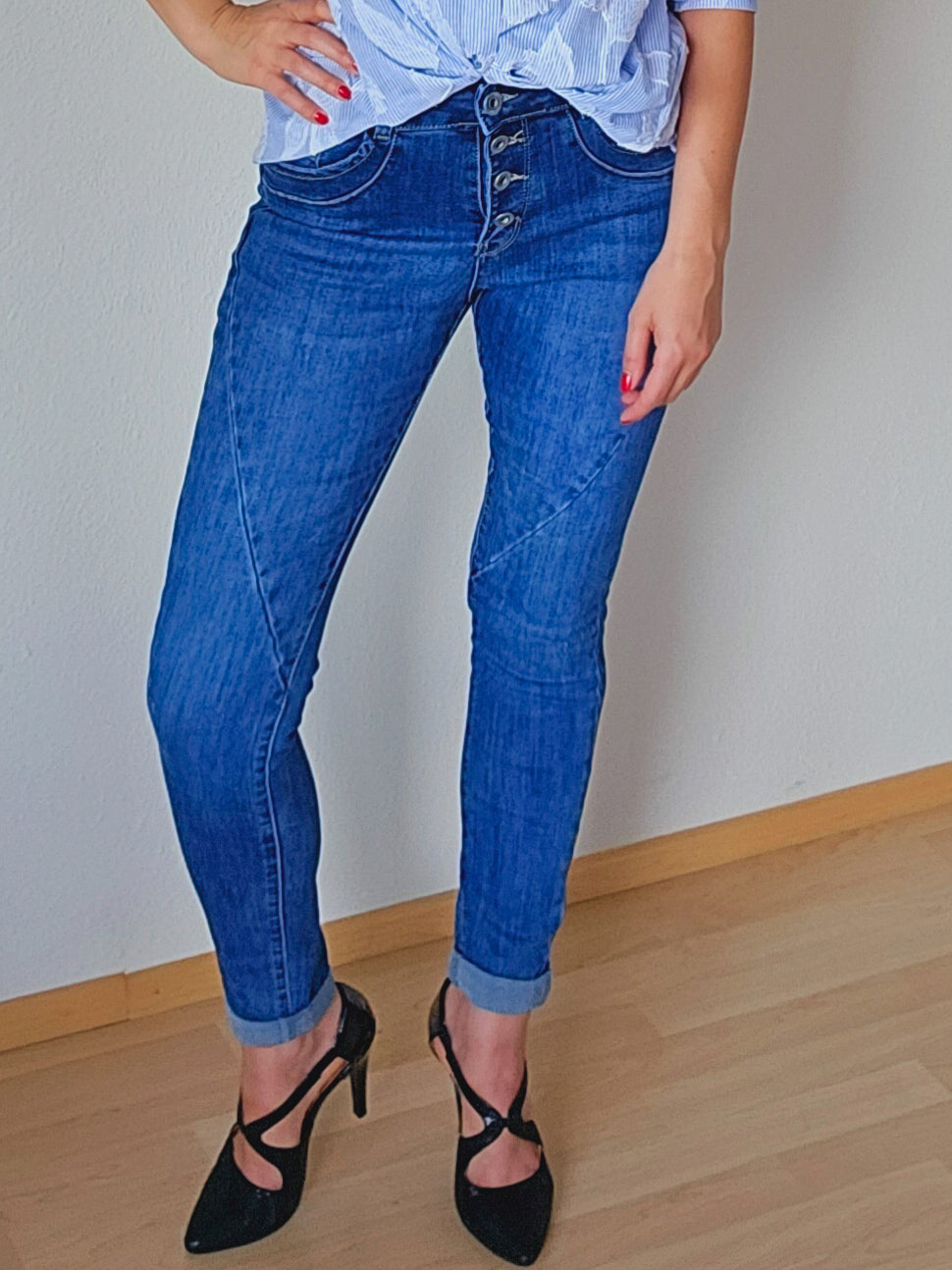 Die Person trägt eine blaue, schmal geschnittene Jeans mit sichtbarer Knopfleiste. Die Jeans ist am Saum leicht umgeschlagen.