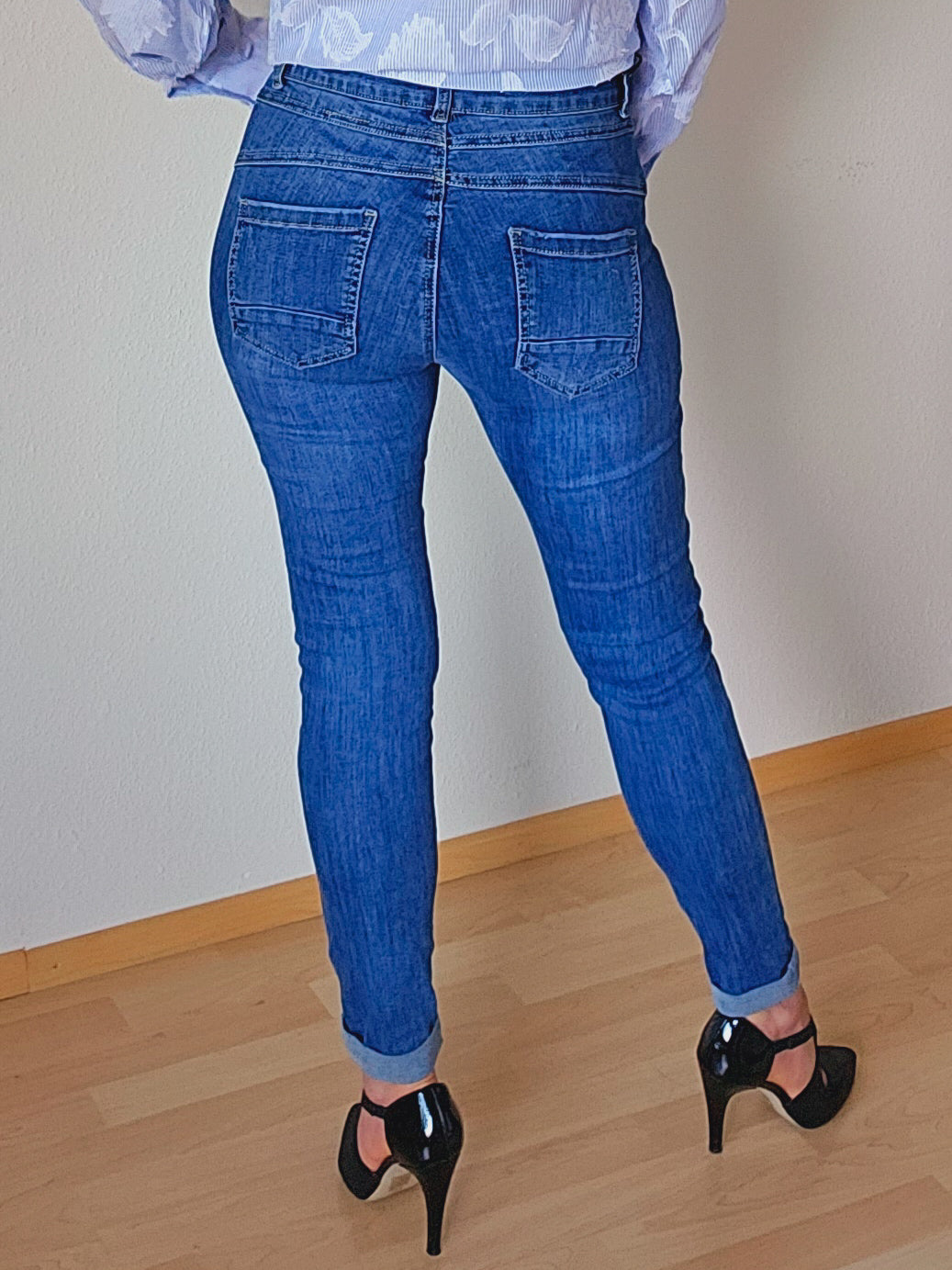 Die Person trägt eine blaue, schmal geschnittene Jeans mit sichtbarer Knopfleiste. Die Jeans ist am Saum leicht umgeschlagen.